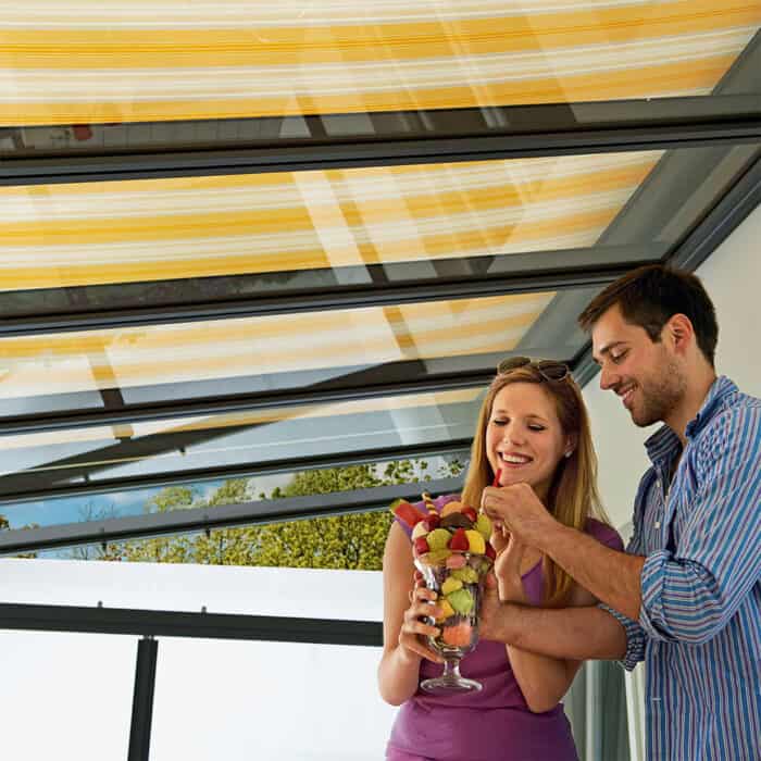 Mann und Frau glücklich auf der Terrasse. Terrassenüberdachung mit Aufglasmarkise.
